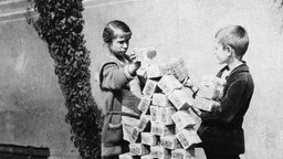 Schwarz-weiß Foto: Kinder stapeln Geldbündel zu großer Pyramide.