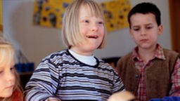 Mädchen mit Down-Syndrom spielt mit nicht behinderten Kindern in einer Vorschule.