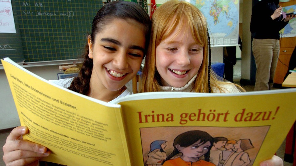 Zwei lachende Schülerinnen lesen in dem Buch &#8222;Irina gehört dazu&#8220;.
