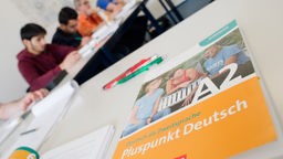 Deutsch-Buch liegt auf Tisch, im Hintergrund Schüler