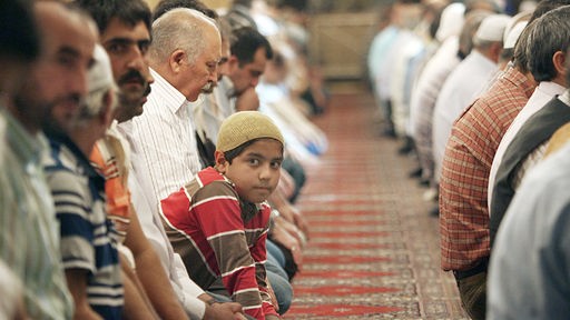 Muslimische Männer und ein Junge knien in einer Moschee.
