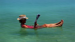 Eine Frau liegt auf dem Rücken im Wasser des Toten Meeres und liest Zeitung.
