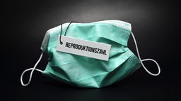 Schutzmaske mit Etikett und Aufschrift "Reproduktionszahl".