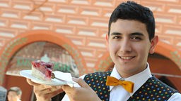 Ein junger Kellner hält einen Teller mit Kuchen.