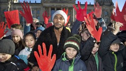 Ein Afrikaner steht zwischen Schülern, die mit roten Händen demonstrieren.