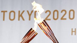 Die olympische Flamme wird vor dem Schriftzug Tokyo 2020 weiter gereicht.