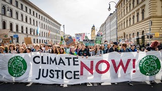 Demonstrant:innen hinter einem Transparent mit der Aufschrift 'Climate Justice Now'.