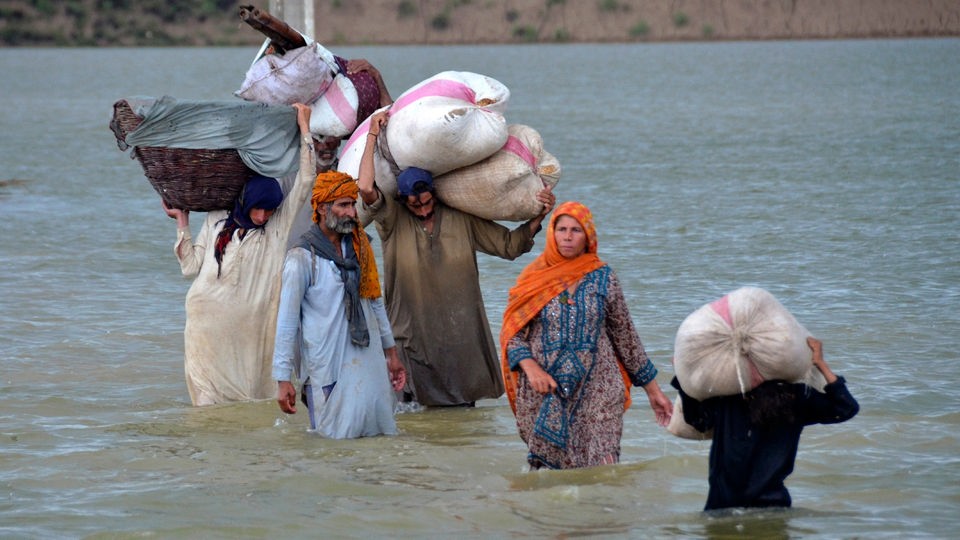 Pakistanische Familie trägt ihr Hab und Gut durch Hochwasser.