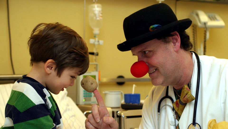Ein Klinik-Clown mit roter Nase spielt mit einem kleinen Patienten.
