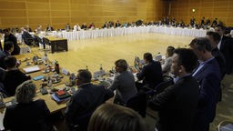 Riesiger Verhandlungstisch mit Teilnehmern an den Koaltitionsverhandlungen.