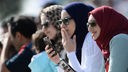 Junge muslimische Frauen mit Kopftüchern, Sonnenbrillen und Handys.