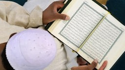 Muslim von oben mit aufgeschlagenem Koran in der Hand.