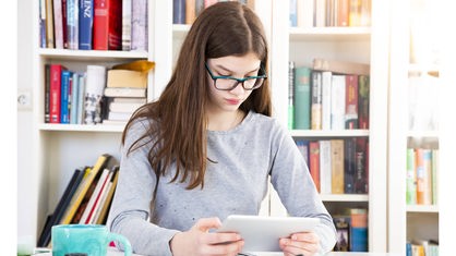 Mädchen mit Brille liest von einem Tablet. 