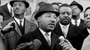 Martin Luther King zwischen anderen Bürgerrechtlern vor Mikrofonen.