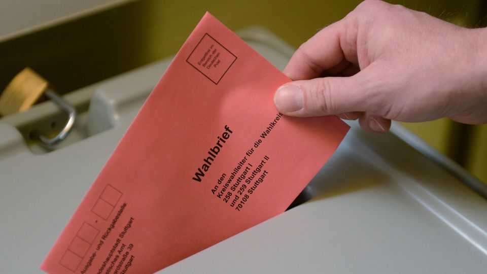 Hand steckt Wahlzettel in eine Wahlurne.