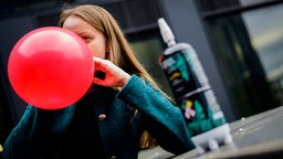 Ein Mädchen atmet aus einem Luftballon ein; daneben steht eine Lachgaskartusche.