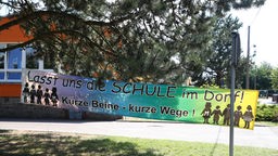 Ein Plakat mit der Aufschrift "Lasst die Schule im Dorf" hängt vor einer Grundschule in Thüringen.