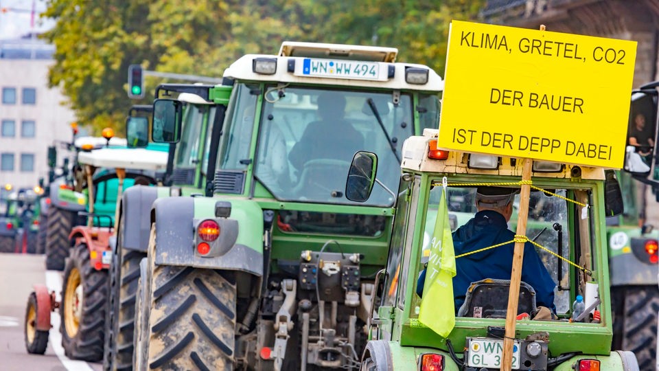 Bauernprotest mit Traktoren, an einem hängt Schild 'Klima, Gretel, CO2 - Der Bauer ist der Depp dabei'.