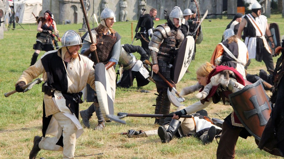 Mittelalterlich gekleidete Rollenspieler kämpfen auf einer Wiese gegeneinander.
