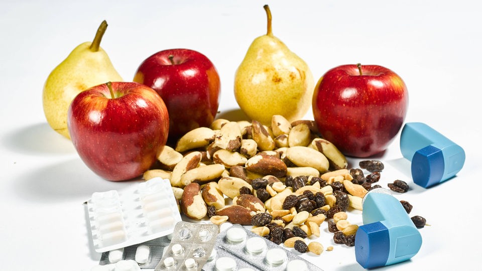 Birnen, Äpfel und Nüsse liegen neben Asthma-Sprays und Tabletten in Blister-Verpackungen.