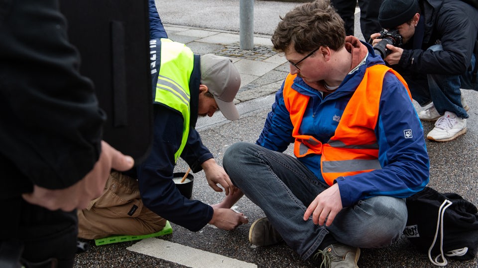 Polizist setzt Speiseöl ein, um die Hand eines Aktivisten von der Straße zu lösen.
