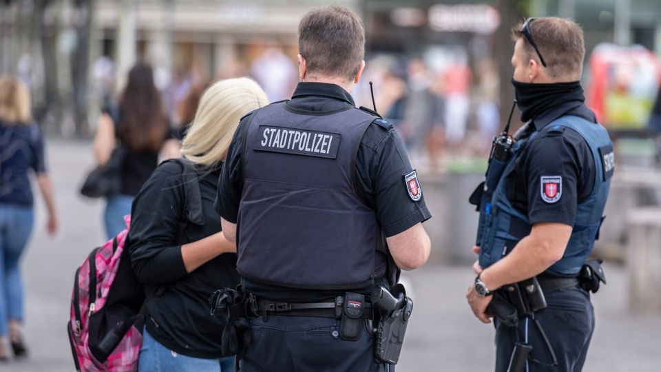 Zwei Polizisten stehen vor einer Frau.