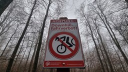 Ein Schild mit der Aufschrift "Achtung! Downhill - Fahrverbot!" steht in einem Waldgebiet.