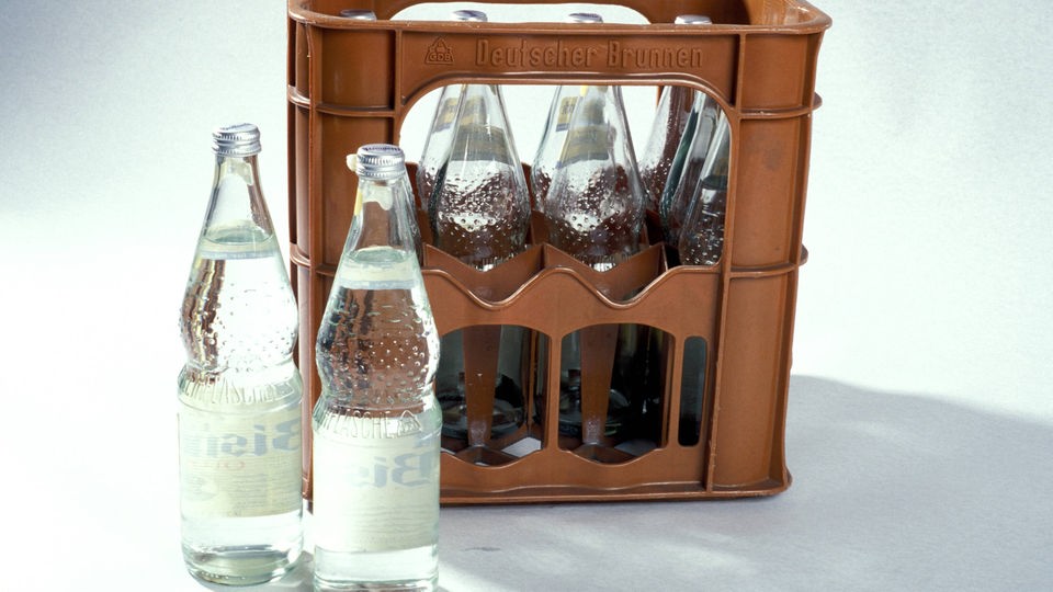 Zwei Perlenflaschen stehen vor einem Kasten mit Mineralwasserflaschen.