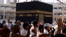 Weiß gekleidete Pilger umrunden die schwarze, würfelförmige Kaaba.