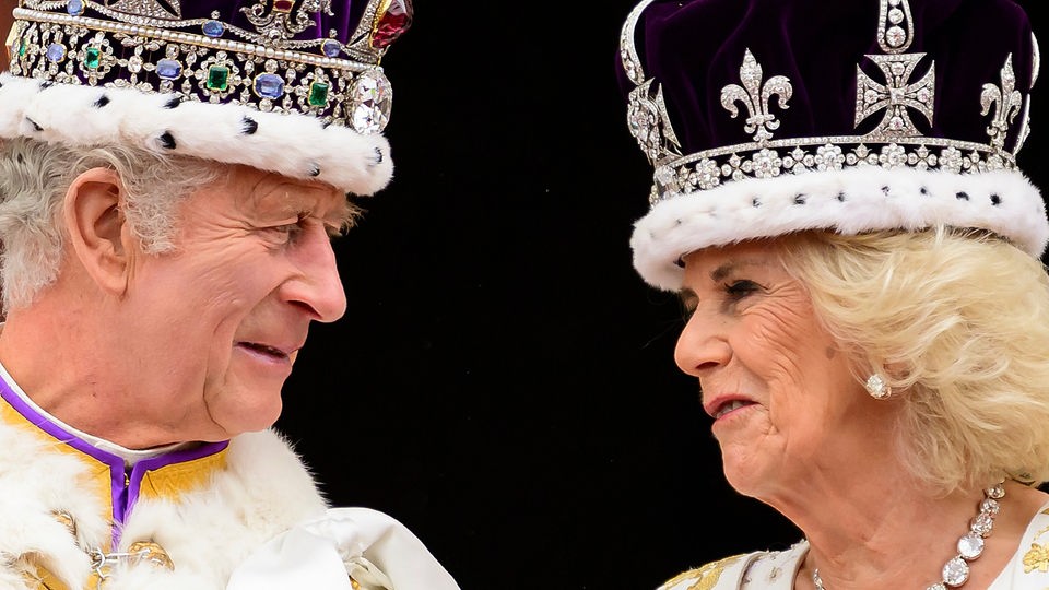 König Charles der Dritte und Königin Camilla mit Kronen auf dem Kopf, schauen sich an.
