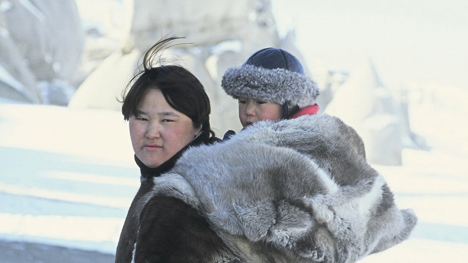 Eine Inuit trägt ihr in Felle gehülltes Kind auf dem Rücken.