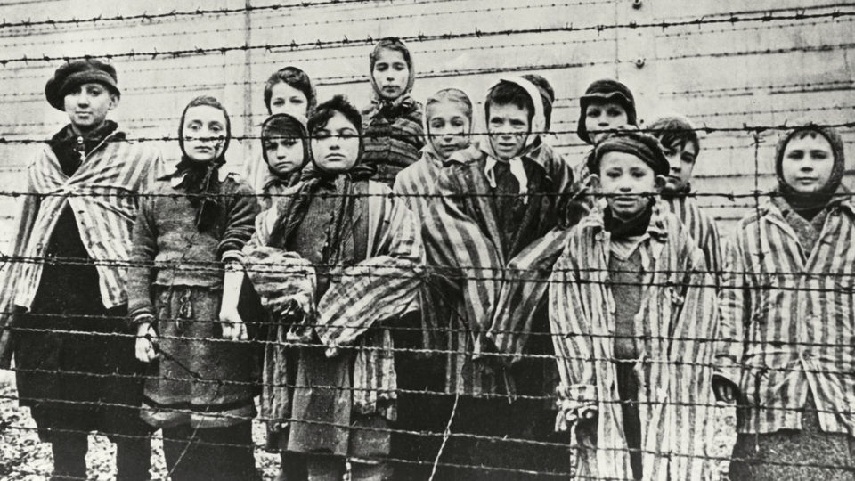 Eine Gruppe Kinder steht im Konzentrationslager Ausschwitz hinter einem Stacheldrahtzaun.