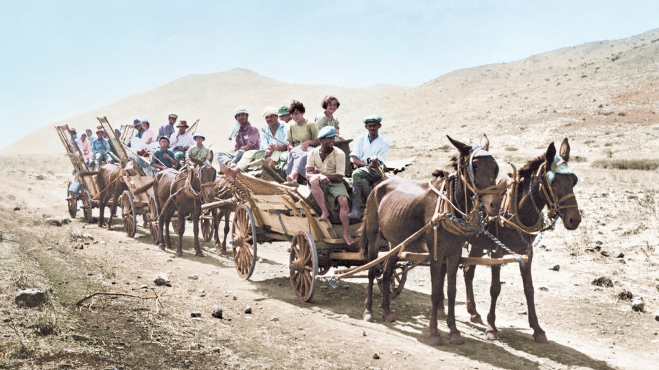 Nachträglich koloriertes Foto: Jüdische Siedler auf Karren, die von Pferden gezogen werden.