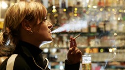 Frau sitzt rauchend an einer Bar.