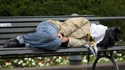 Ein Obdachloser schläft auf einer Parkbank.