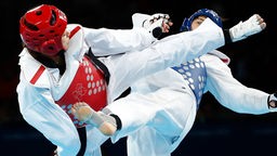 Zwei Frauen in weißen Taekwondo-Anzügen kämpfen gegen einander.
