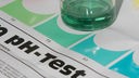 ph-Wert-Test: Ein Messbecher mit grün gefärbter Testflüssigkeit steht auf einem Testformular.