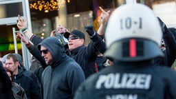Polizist beobachtet Pegida-Demonstranten in Köln, die den Mittelfinger hoch strecken.