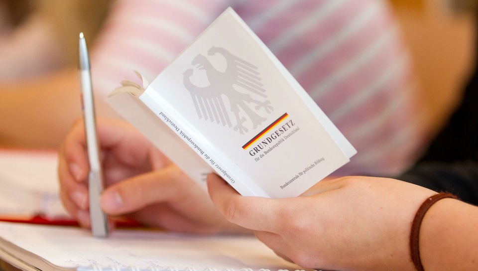 Hand hält kleine Ausgabe des Deutschen Grundgesetzes.