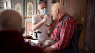 Ein Pfleger mit Mund-Nasen-Schutz füttert einen alten Mann.