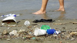Nackte Füße laufen über Strand mit Plastikmüll.