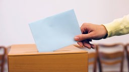 Hand steckt Brief in eine Wahlurne.