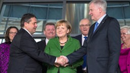 Der SPD-Vorsitzende Sigmar Gabriel und der Vorsitzende der CSU Horst Seehofer geben sich vor Angela Merkel die Hand.