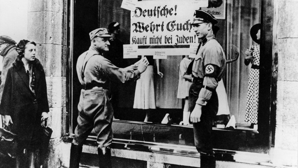 Zwei SA-Mitglieder hängen ein Schild mit der Aufschrift Deutsche! Wehrt Euch! Kauft nicht bei Juden an ein Schaufenster.