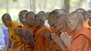 Buddhistische Mönche in orangenen Roben sitzen mit verschränkten Händen nebeneinander und beten