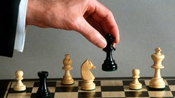 Eine Männerhand macht mit der schwarzen Dame einen Zug auf dem Schachbrett.