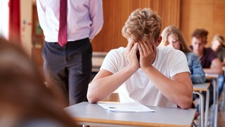 Ein verzweifelter Schüler hält sich die Hände vor sein Gesicht.