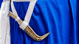 Kirpan ist mit weißen Bändern über blauem Kleidungsstück befestigt.