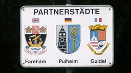 Schild mit Schriftzug "Partnerstädte" Wappen der