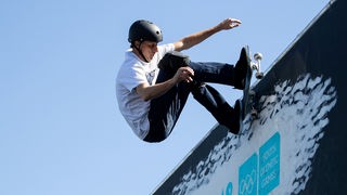 Skater Tony Hawks mit seinem Skateboard an der oberen Kante einer steilen Bowl. 